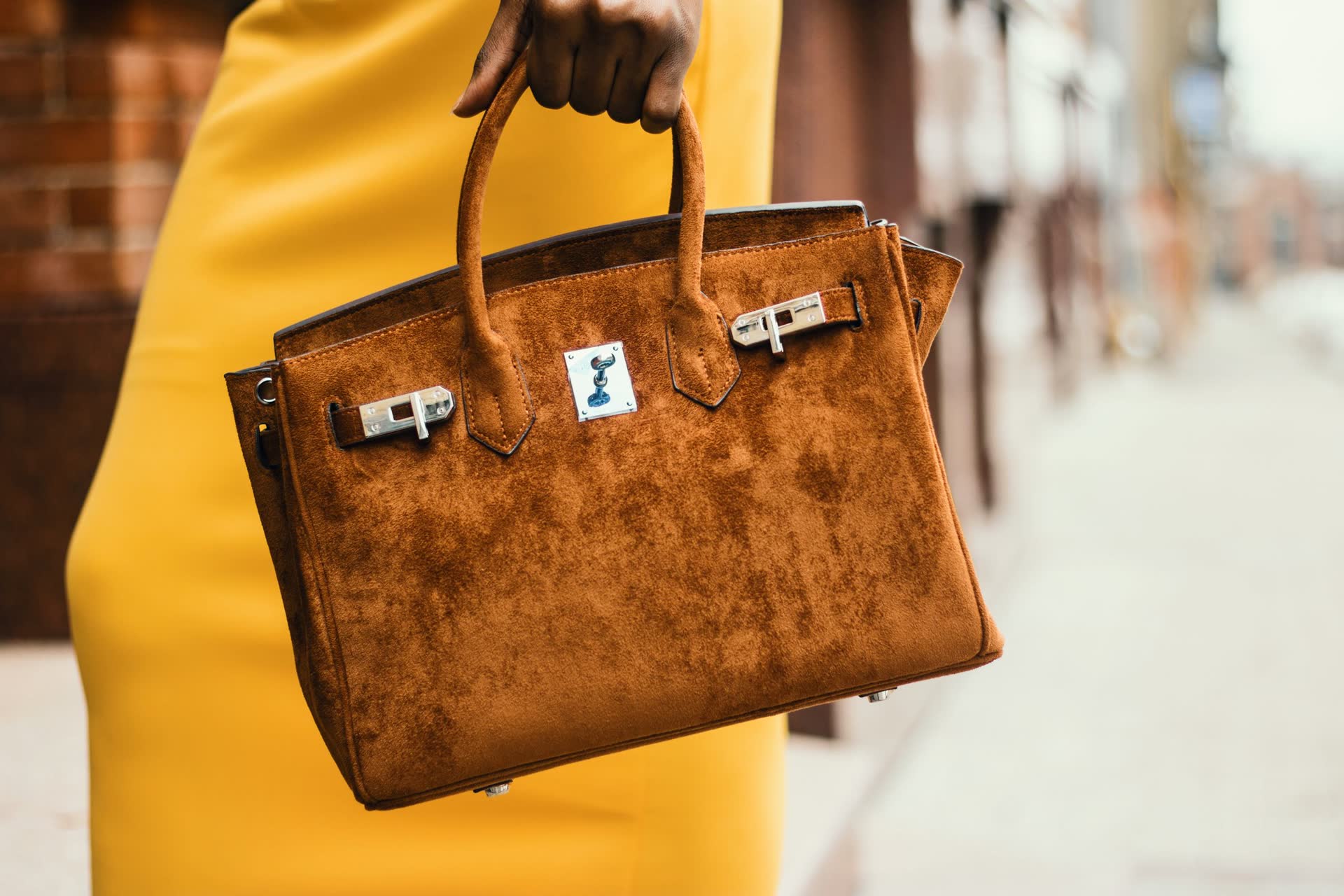 Model in a yellow coat carrying a brown suede leather handbag