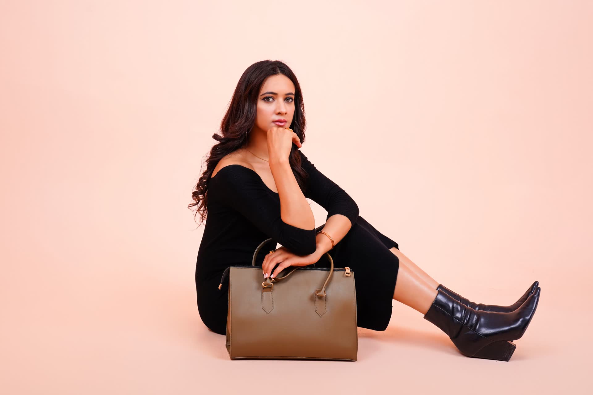 Model in black sitting beside a brown leather handbag